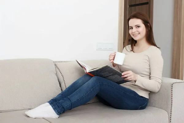 집에 앉아 있는 젊은 여자가 거실에서 편안하게 책을 읽고 있는 모습 — 스톡 사진