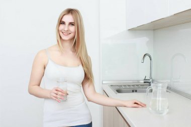 güzel bir genç kadın bir bardak su ile mutfak üzerinde tutar.