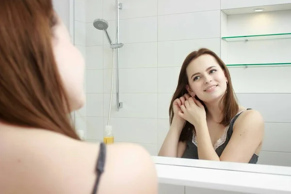 Concepto de la mañana y la gente - mujer joven mirando al espejo en el baño en casa — Foto de Stock