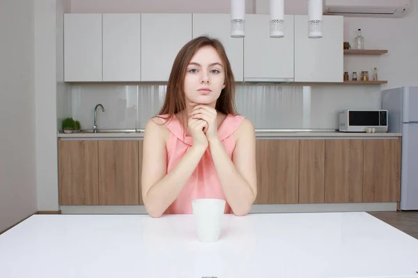 Mulher sorridente que sentado na cozinha com xícara de café e olhando para a câmera — Fotografia de Stock