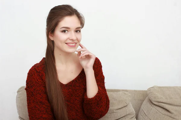 Vacker flicka i röd tröja sitter på soffan poserar och leende — Stockfoto