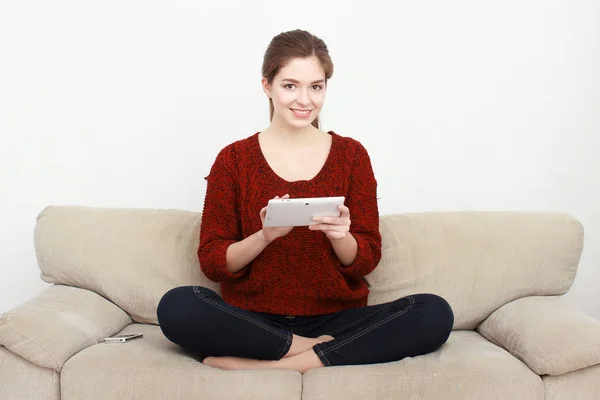 Belle fille utilise une tablette numérique et souriant tout en étant assis sur le canapé à la maison — Photo