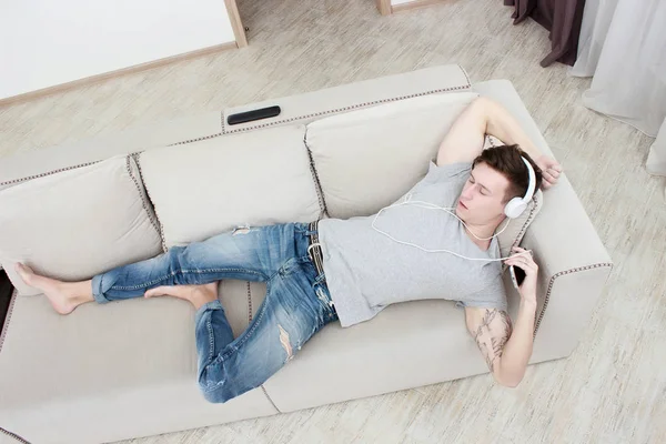 Mann zu Hause auf Sofa und hört Musik mit Smartphone — Stockfoto