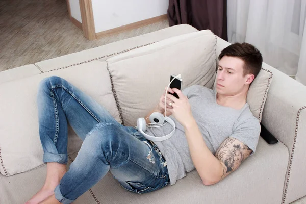 Mann hört Musik mit Kopfhörer und Smartphone, während er es sich auf Sofa gemütlich macht — Stockfoto