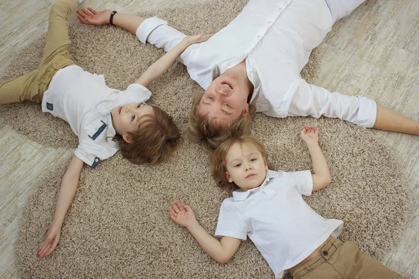 Vista dall'alto del giovane padre con simpatici figlioletti sdraiati sul pavimento — Foto Stock
