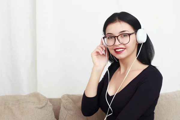 Jovem menina retrato sentado em um sofá, ouvir música em fones de ouvido . — Fotografia de Stock