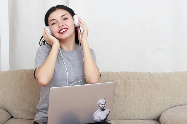 Nő segítségével a laptop számítógép és a fejhallgató, ül a nappaliban — Stock Fotó