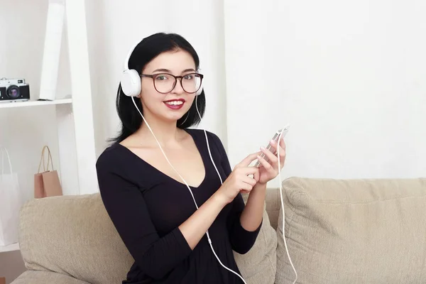 Young girl portrait sitting on a sofa, listen music in headphones. — Stock Photo, Image