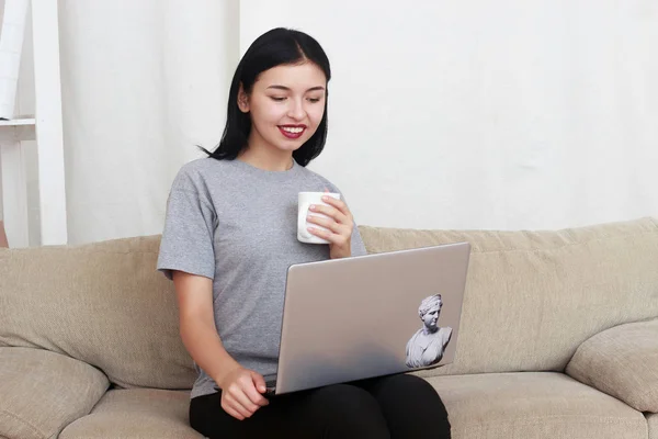 Hübsche junge Frau arbeitet an einem Laptop, während sie Tee trinkt — Stockfoto