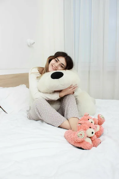 Joven chica hermosa en la cama. Alegre, feliz, cama con un oso de juguete grande . — Foto de Stock