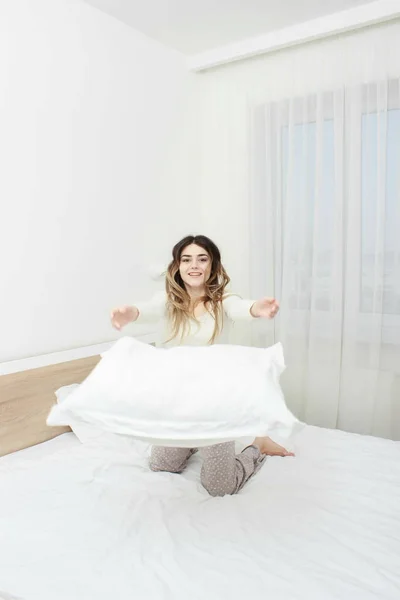 Kadın gülümsüyor ve yastık atma pijama — Stok fotoğraf