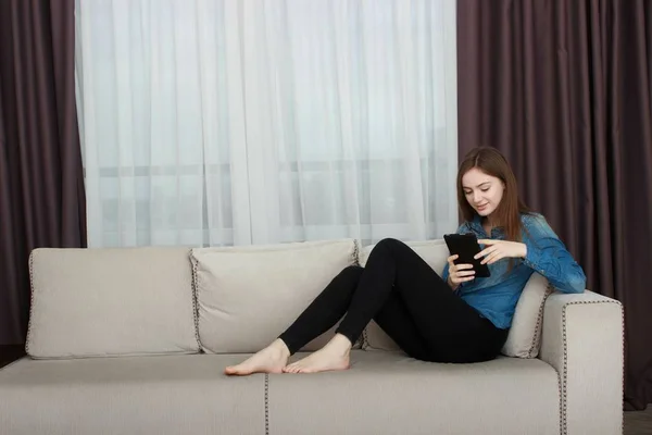 Woman relaxing on sofa while touching a tablet in a living room — Stock Photo, Image