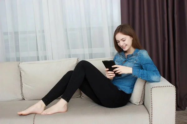 Kvinne som slapper av på sofaen mens hun tar på en tablett i stua – stockfoto