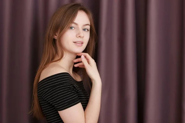 Chica joven con vestido negro contra cortinas. Mirando a la cámara — Foto de Stock