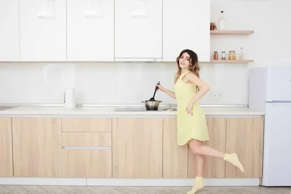 Кулинария женщина в желтом платье на кухне с пластиковой ложкой . — стоковое фото
