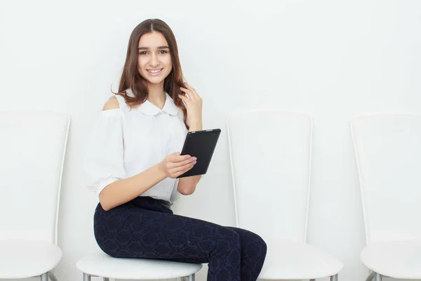 Jeune fille assise sur une chaise et utilisant une tablette — Photo