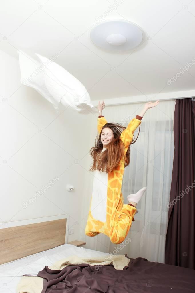 Funny girl in kigurumi pajamas jumping on the bed