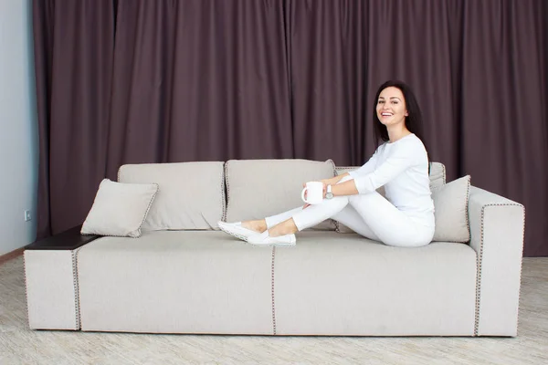 Porträt einer schönen jungen Frau, die zu Hause mit einer Tasse Tee auf dem Sofa sitzt — Stockfoto