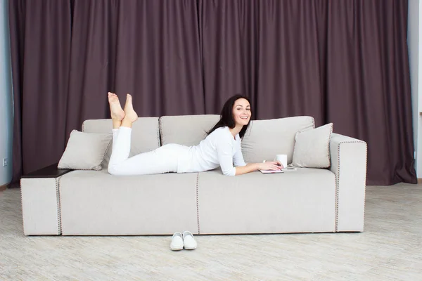Портрет красивой молодой женщины, лежащей дома на диване с чашкой чая — стоковое фото