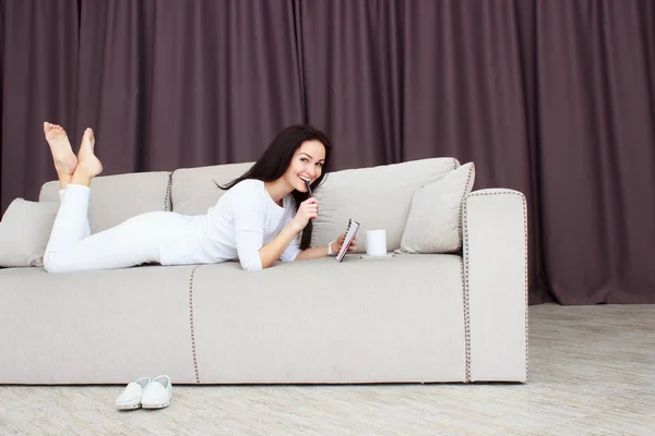 Porträt einer schönen jungen Frau, die zu Hause mit einer Tasse Tee auf dem Sofa liegt — Stockfoto