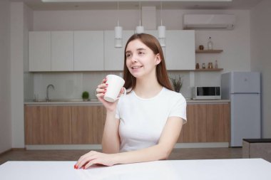 Kahve fincanı ile mutfakta oturmuş gülümseyen kadın. Uzun saçlı güzel kız