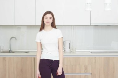 Genç ve güzel kadın mutfakta ayakta ve gülümseyen bir beyaz T shirt.