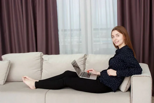 Attractive young woman using a digital tablet while relaxing on a sofa — Stock Photo, Image