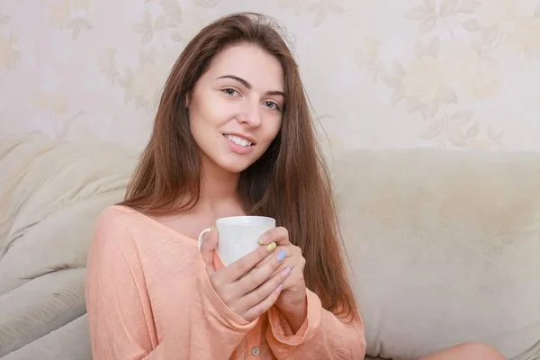 Mutlu genç kadın kahve ile rahat giysiler içinde kanepede oturan — Stok fotoğraf