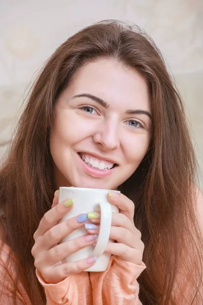 快乐的年轻女人坐在杯咖啡舒适布放在沙发上 — 图库照片