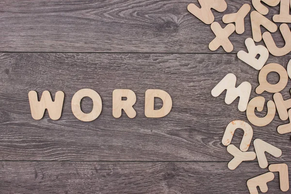Slovo z dřevěné písmena vedle hromadu dalších písmen za dřevěné desky — Stock fotografie