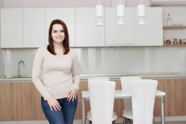 Ciddi tutum. Genç gülümseyen Bayan bir mutfakta ayakta.