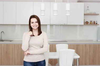 Ciddi tutum. Genç gülümseyen Bayan bir mutfakta ayakta.