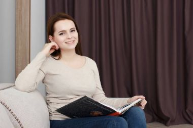 Güzel gülümseyen genç kadın kanepe üzerinde rahatlatıcı bir kitap zevk