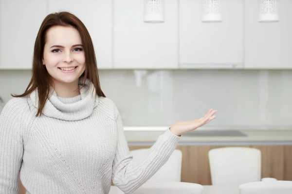 Serious attitude. Young smiling lady standing in a kitchen.
