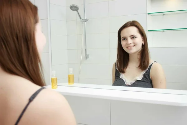 Concepto de la mañana y la gente - mujer joven mirando al espejo en el baño en casa — Foto de Stock