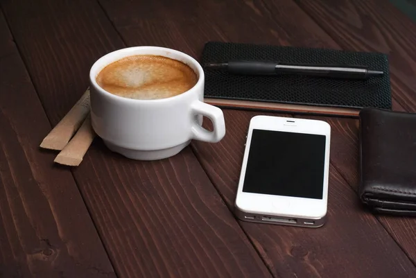 Smartphone with notebook and cup of strong coffee on wooden background — Stock Photo, Image