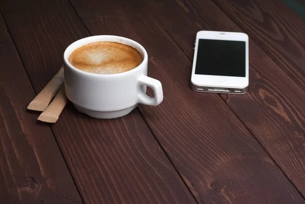 Κάτοψη του φλιτζάνι καφέ με μοτίβο καρδιά σε ένα λευκό φλιτζάνι και έξυπνο τηλέφωνο σε φόντο ξύλινη — Φωτογραφία Αρχείου