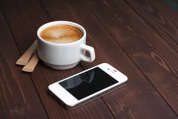 Κάτοψη του φλιτζάνι καφέ με μοτίβο καρδιά σε ένα λευκό φλιτζάνι και έξυπνο τηλέφωνο σε φόντο ξύλινη — Φωτογραφία Αρχείου