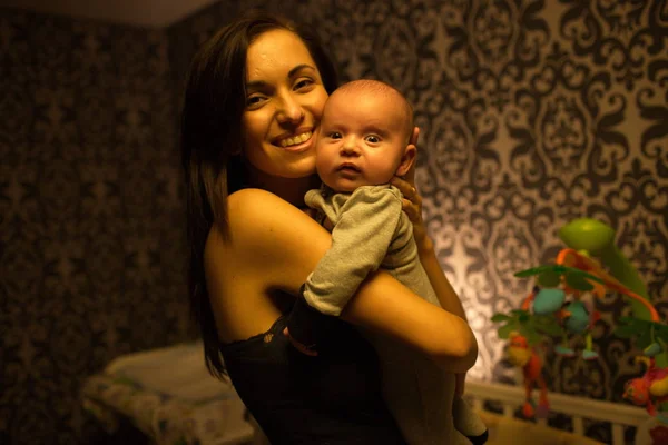 Улыбающаяся молодая мать держит своего маленького мальчика в спальне — стоковое фото