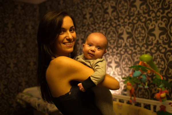Uśmiechnięta młoda matka trzyma jej mały chłopiec w sypialni — Zdjęcie stockowe