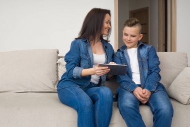 Mutlu aile kanepede oturan ve evde dijital tablet kullanma