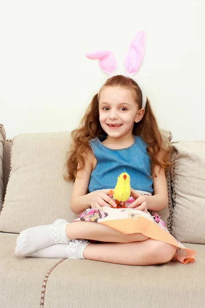 Söt liten flicka med bunny öron och gosedjur som sitter på soffan — Stockfoto
