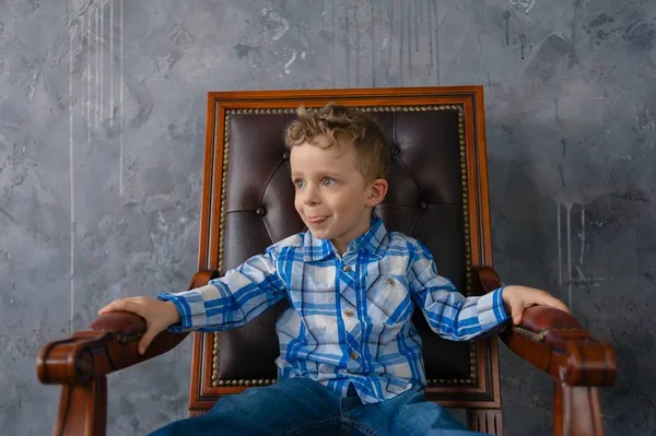 Стильный мальчик в клетчатой рубашке сидит в дизайнерском кресле — стоковое фото