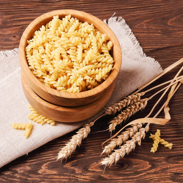 Raw pasta rotini and rye ears in a wooden bowl — Stock Photo, Image