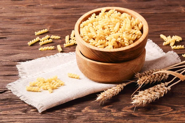 Raw pasta rotini and rye ears in a wooden bowl — Stock Photo, Image