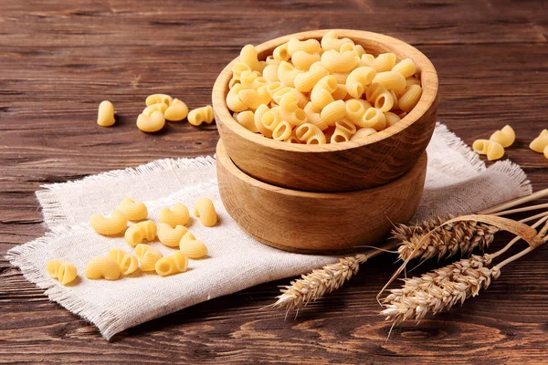 Raw elbow macaroni and rye ears in a wooden bowl