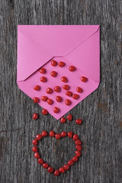 粉红色的信封在木表面与红色糖果心脏 — 图库照片