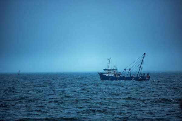 Траулерская рыбацкая лодка, плывущая в открытых водах на холодном и туманном
 
