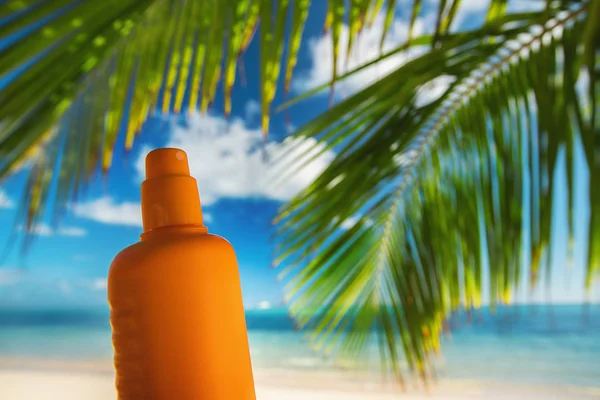 Bottle of sun protection lotion and palm leaf on the background