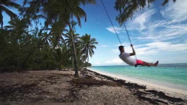 Hombre en un columpio en la playa de la isla tropical disfrutando de sus vacaciones de verano — Vídeo de stock